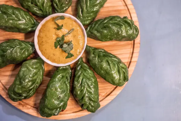 Green spinach momo arranged on a wooden board with achar