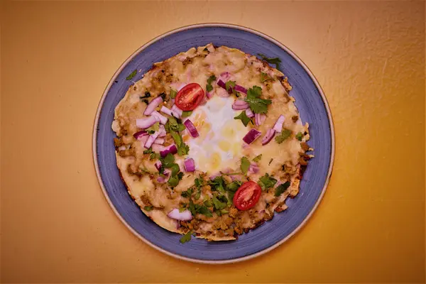 Chatamari, the Nepalese rice crepe, topped with egg, tomato and red onion